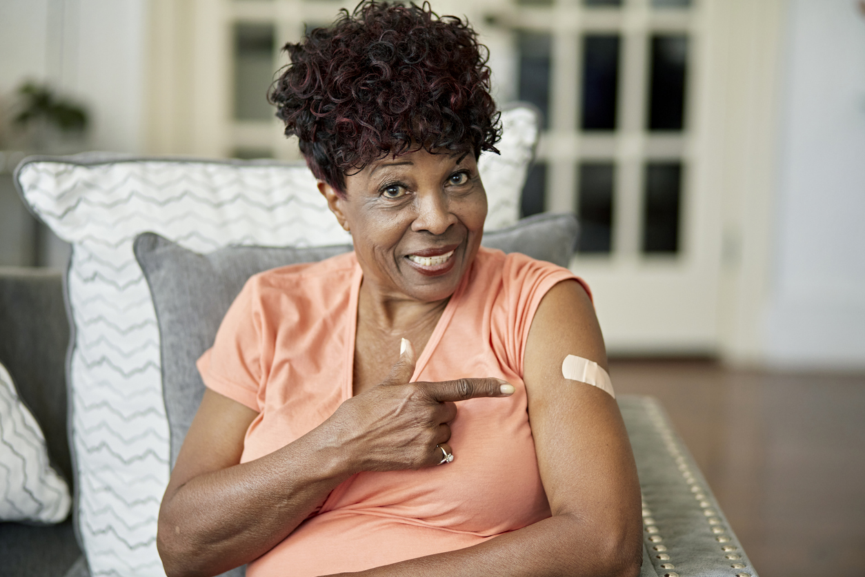 woman of African descent smiles and points to a bandaid on her upper arm where she received a vaccination