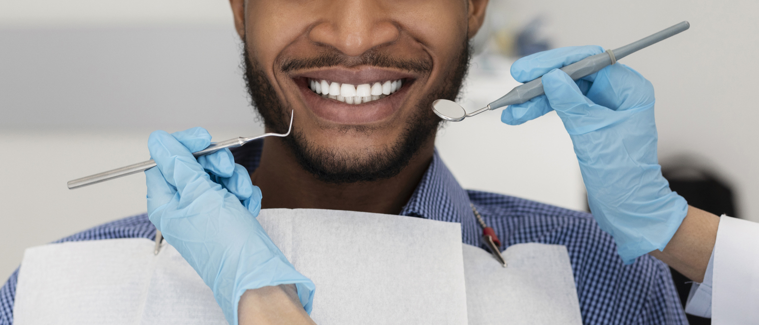 A dentist or dental hygienist's hands in protective gloves with tools and smiling patient black man