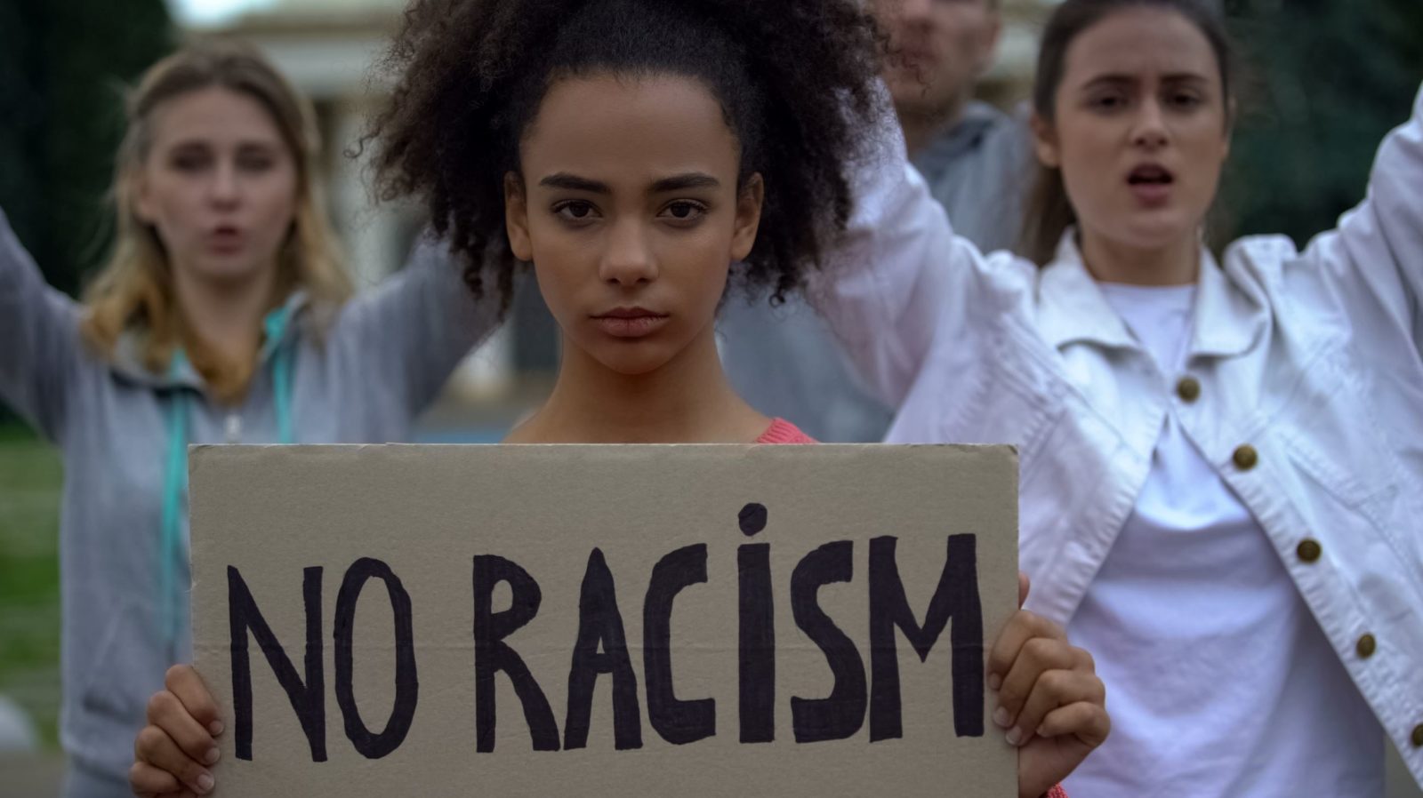 young Black person at a rally holds a sign that says "no racism"