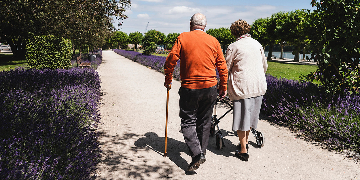 Older couple walking in park, woman using wheeled walker