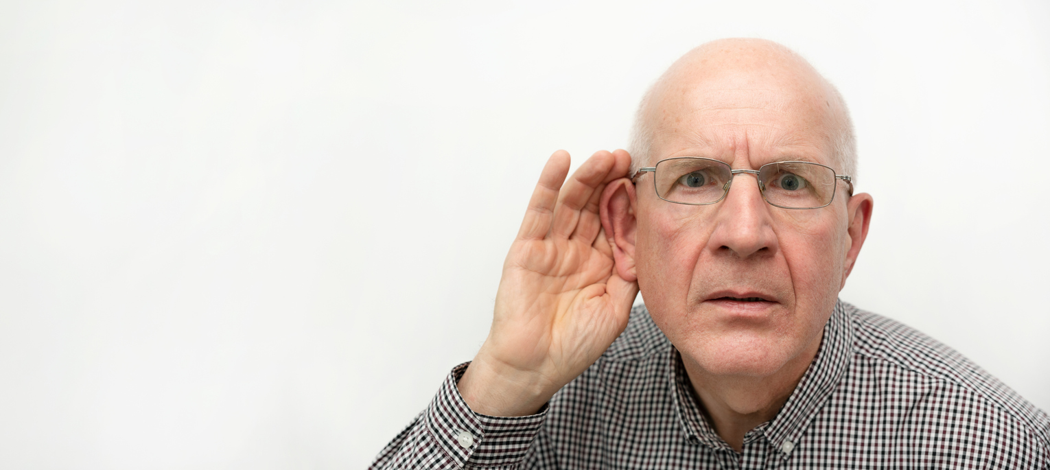 older white man with his hand cupped around one ear in order to hear better