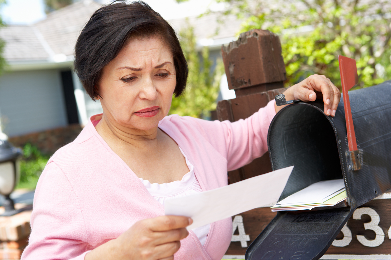 older Latina looks worried about something she received in her mailbox