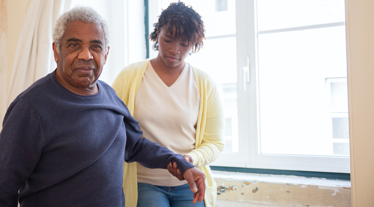 older African American man receives support walking from a younger African American woman