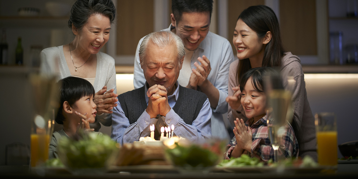 family gathered around older man about to make a wish over a birthday cake
