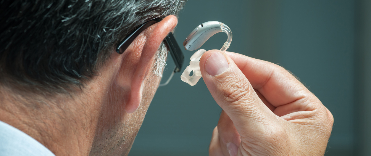 man about to place a hearing aid behind and in his ear