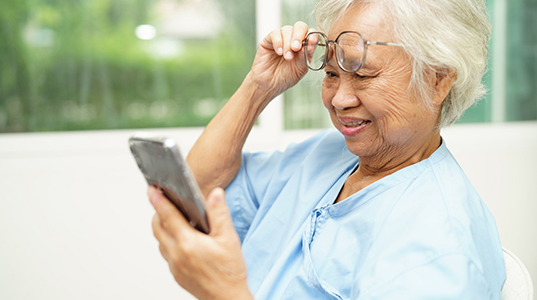 older Asian woman lifting glasses to better read her smart phone
