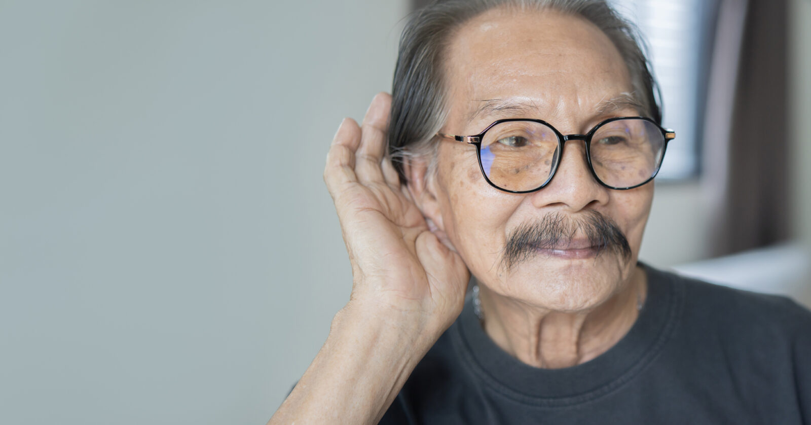 older Asian man cupping his ear to hear