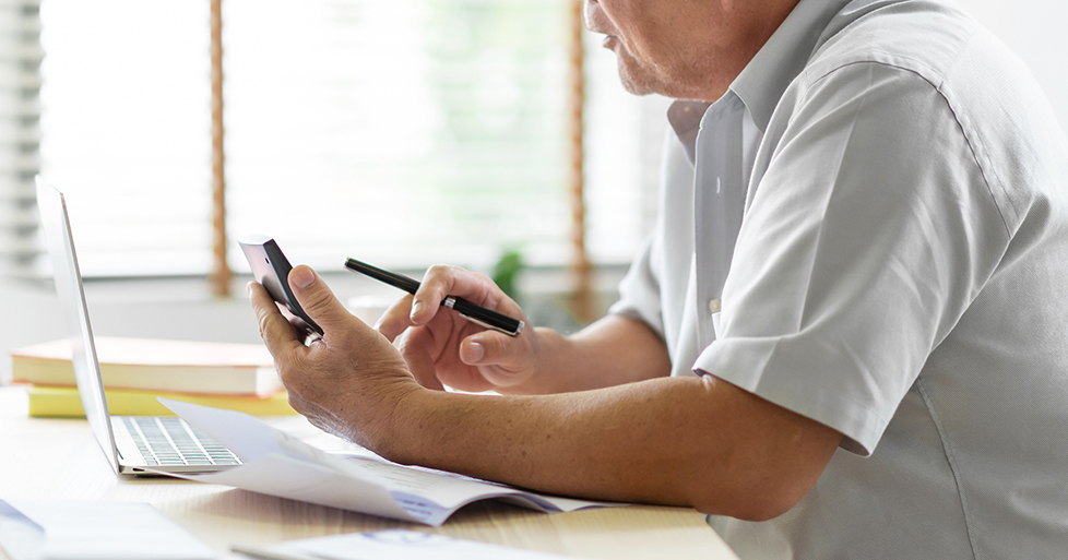 older man calculating finances with handheld calculator, pen, and laptop computer