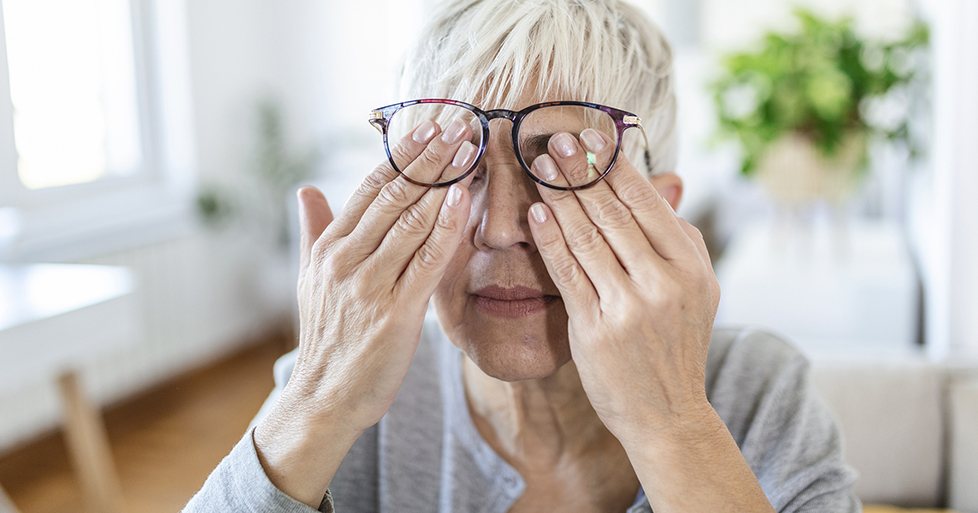 older woman rubs her eyes behind large glasses